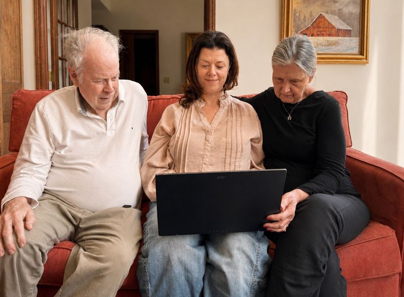 Kathleen Hustad, founder of LightWell Care, sits on a couch with her mother and father, the three of them looking together at a laptop.